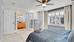 Ein Schlafzimmer mit einem Bett, einem Deckenventilator, einer Kommode und einem Fenster mit Vorhängen.