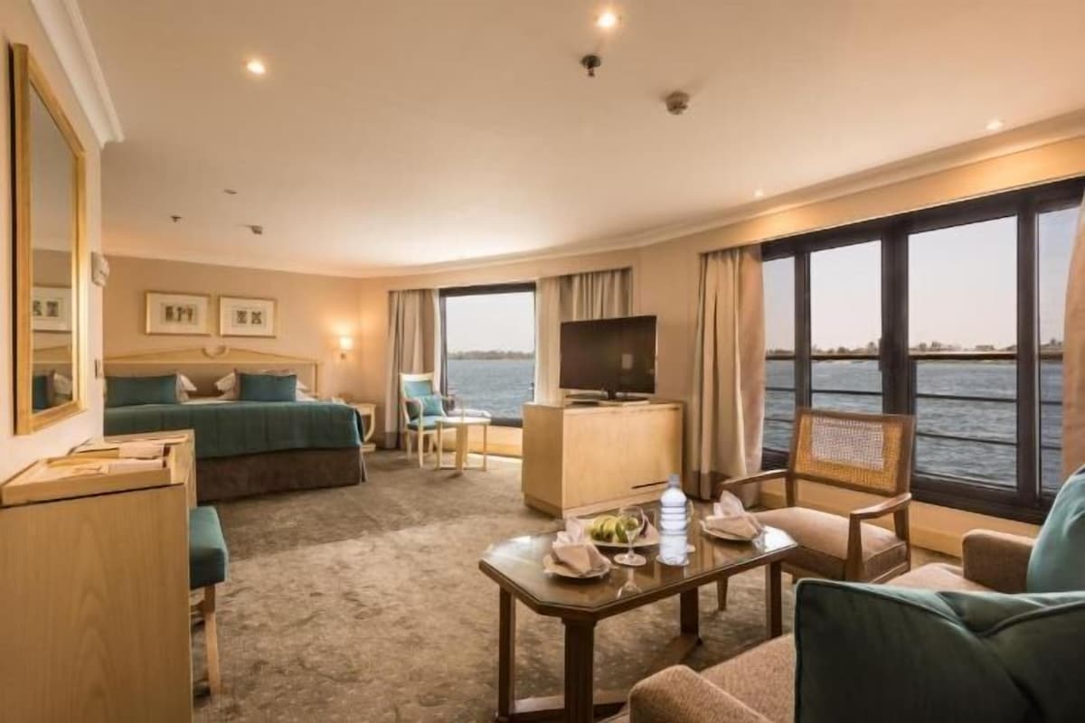 Habitación de hotel con cama, escritorio, televisión, ventana con vista al agua y una silla.