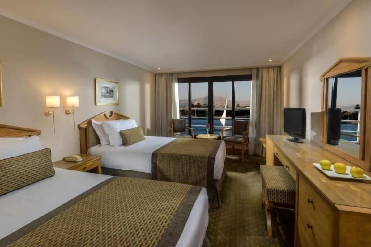 Habitación de hotel con dos camas, un escritorio, una silla, un televisor y vista al mar.