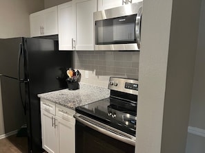 Una cocina con un refrigerador negro, microondas de acero inoxidable y horno.
