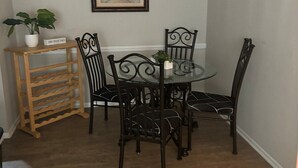 A dining area with a round glass table, four black chairs, a wooden wine rack, and a hanging light fixture.