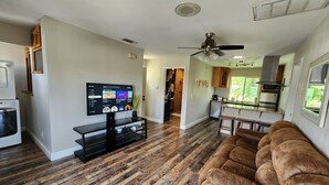 Een moderne woonkamer met een flatscreen televisie, houten vloeren, een bruine leren bank en een keuken met een bar.