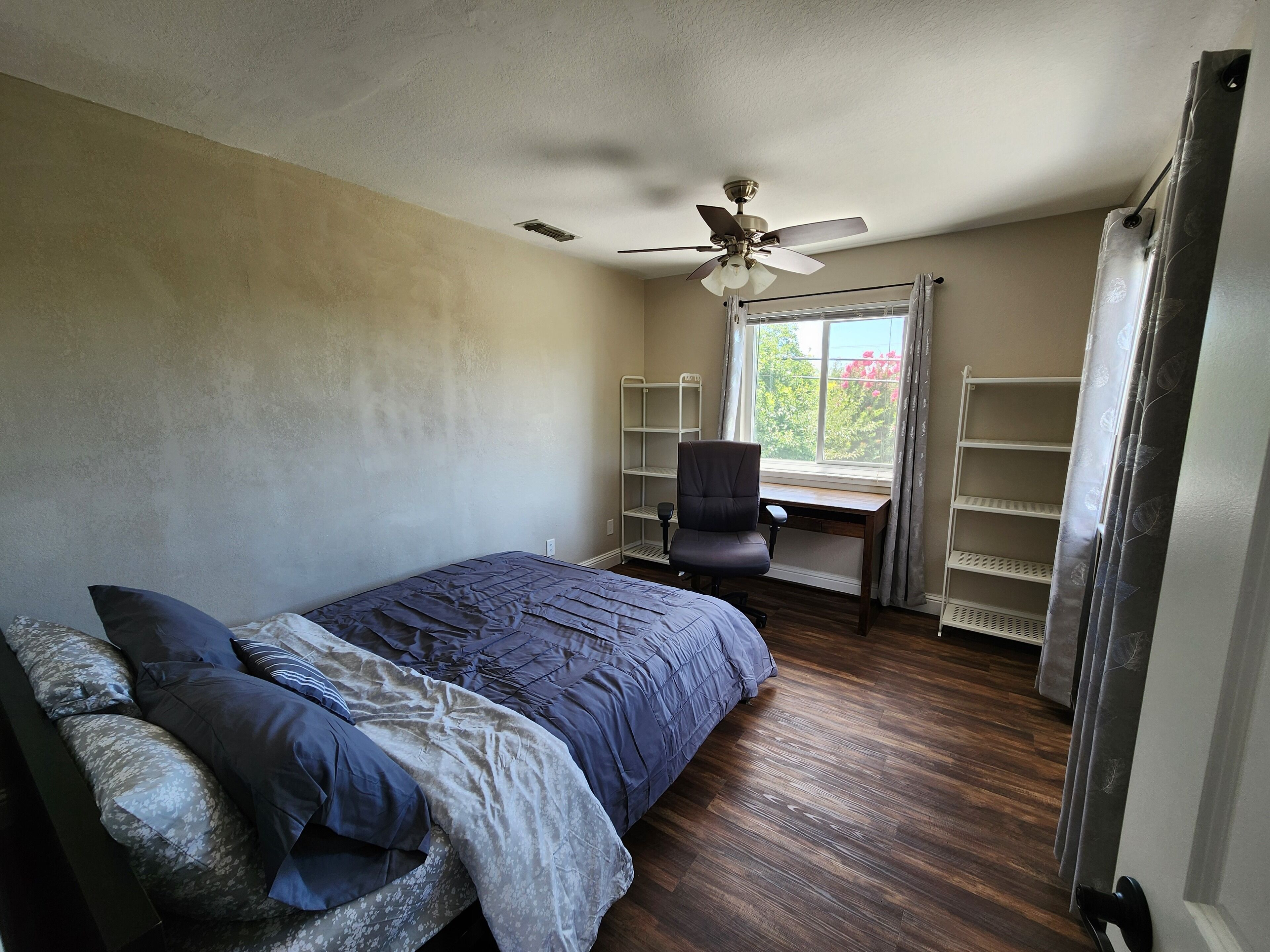 A bedroom with a bed, a desk, a chair, and a ceiling fan.