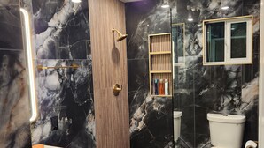 Een moderne badkamer met douche, toilet, wastafel en marmeren wanden.