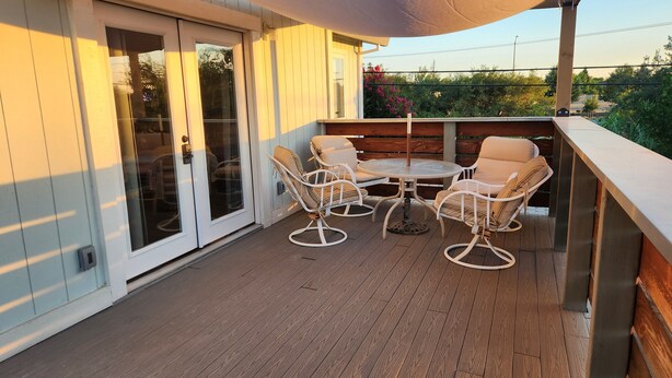 Een overdekt terras met een tafel en stoelen, een schuifpui en uitzicht op groen.