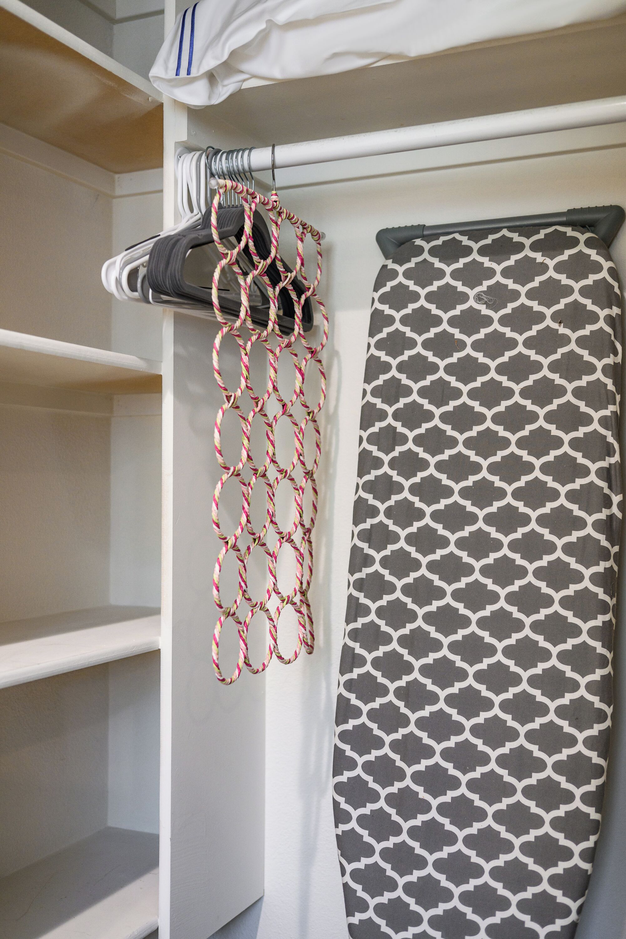 A neatly organized closet with shelves, a hanging rack, and an ironing board.