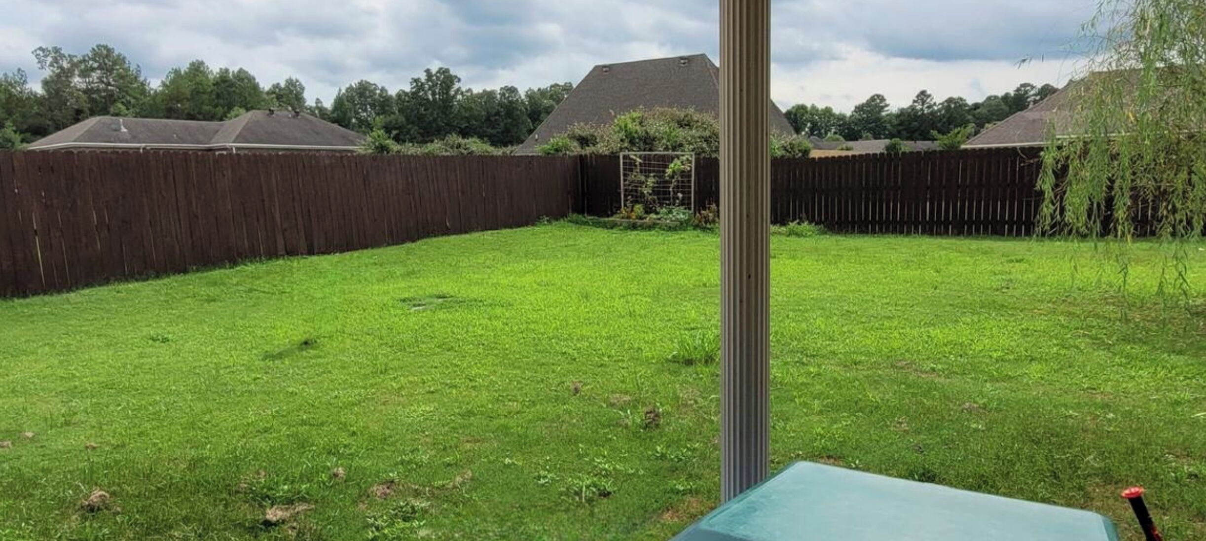 A backyard with a wooden fence, a metal pole, and a green table.