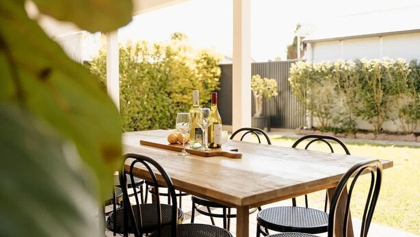 An outdoor dining area with a wooden table and chairs, surrounded by greenery. - Pet Friendly 3 Bed Home w Workspace & Creek Views (Tighes Hill)