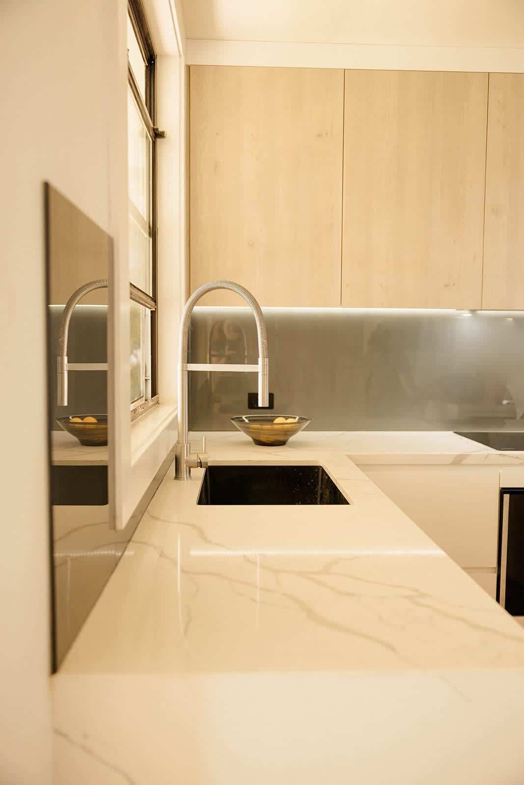 A modern kitchen with a marble countertop, a sink with a vessel sink, and wooden cabinetry.