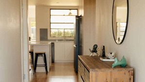 A hallway with wooden flooring, a wooden dresser with drawers, a mirror, and a hanging light fixture. - Pet Friendly 3 Bed Home w Workspace & Creek Views (Tighes Hill)