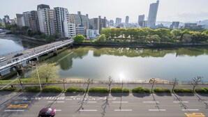A river with a bridge, a parking lot, and a cityscape with buildings. - LIT Hiroshima Ekimae (Hiroshima)