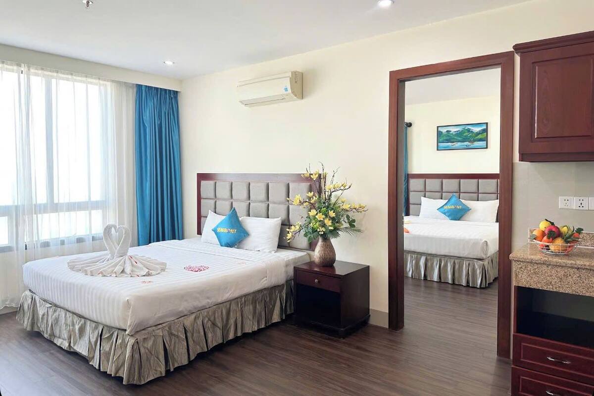 A hotel room with a large bed, a nightstand, a vase with flowers, and a painting on the wall.