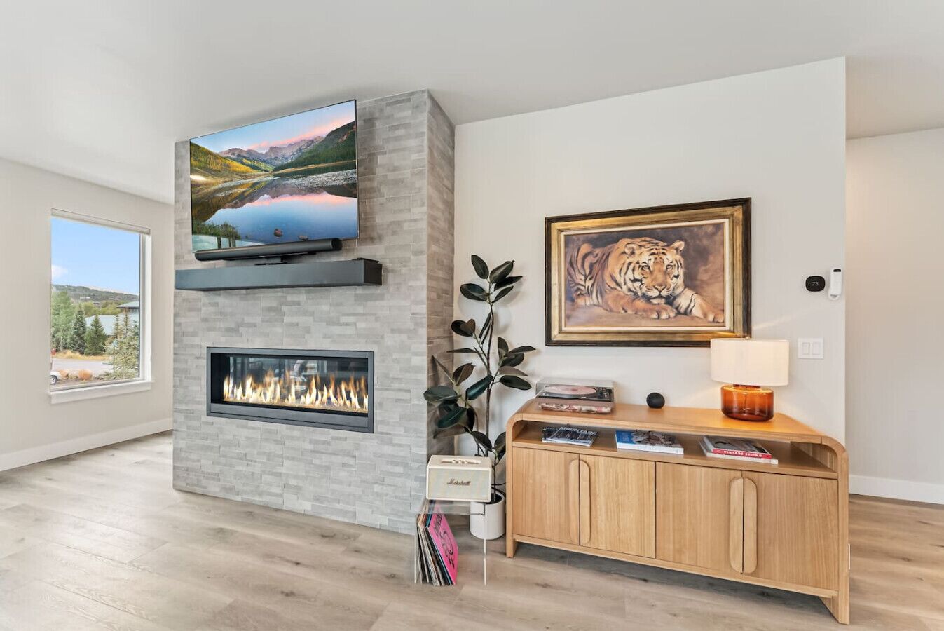 Een moderne woonkamer met een open haard, een wandtelevisie en een houten console met boeken en decoratieve objecten.