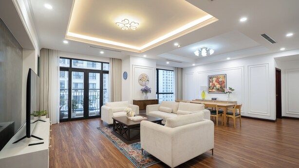 Amplia sala de estar con un televisor de pantalla plana, dos sofás blancos, una mesa de centro de madera y una mesa de comedor con sillas.