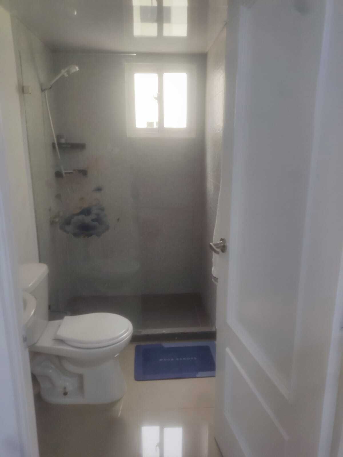 Et lille, aflangt badeværelse med toilet, bruser og et vindue.