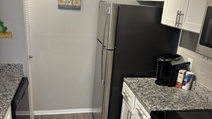 A compact kitchen with white cabinets, a stainless steel refrigerator, a black oven, and a granite countertop. - Cozy Vinings Hideaway 6 (Marietta)