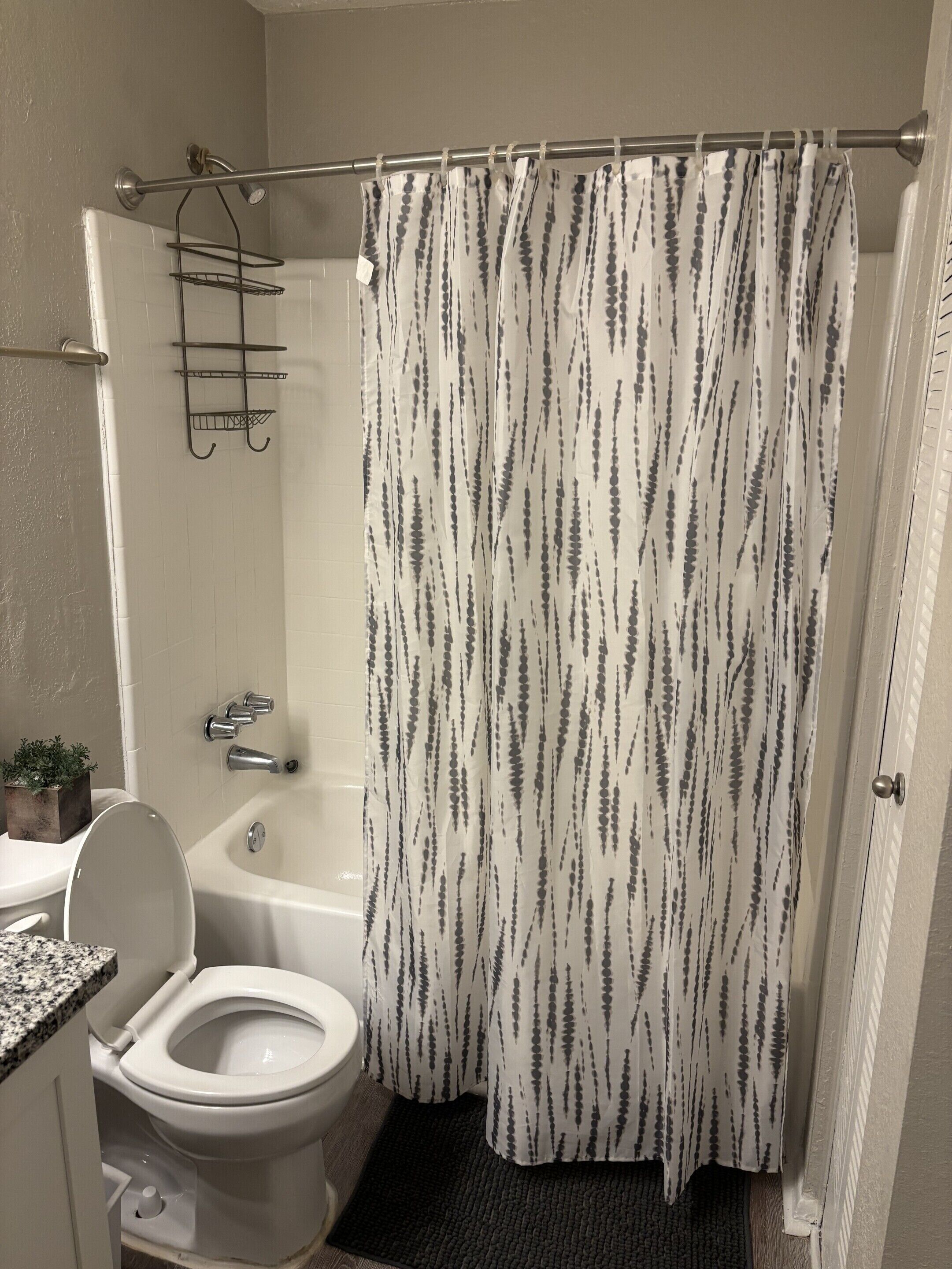 A bathroom with a shower curtain, a bathtub, a toilet, and a sink.