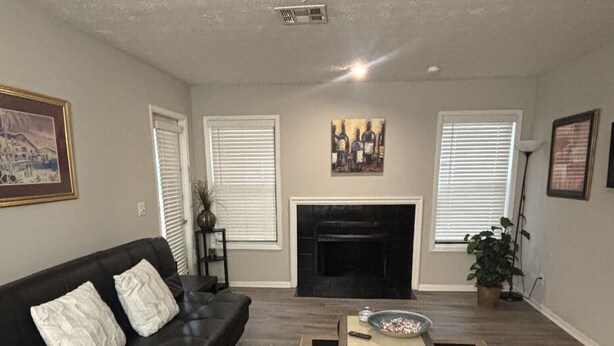 A living room with a black leather sofa, a coffee table, a fireplace, and a painting on the wall. - Cozy Vinings Hideaway 6 (Marietta)