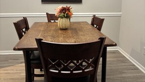 A dining room with a wooden table and chairs, a vase with flowers, and a painting on the wall. - Cozy Vinings Hideaway 6 (Marietta)
