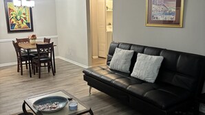 A living room with a black leather sofa, a dining table with chairs, a coffee table, and artwork on the walls. - Cozy Vinings Hideaway 6 (Marietta)