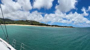 A clear view of turquoise waters, a sandy beach, and a hilly landscape with buildings.