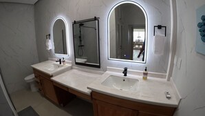 A modern bathroom with two sinks, a shower, and three mirrors.