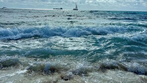 A beach with waves and a sailboat in the distance.