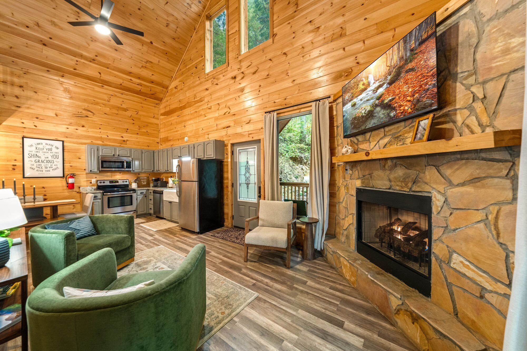 A log cabin interior with a stone fireplace, kitchen, and seating area.