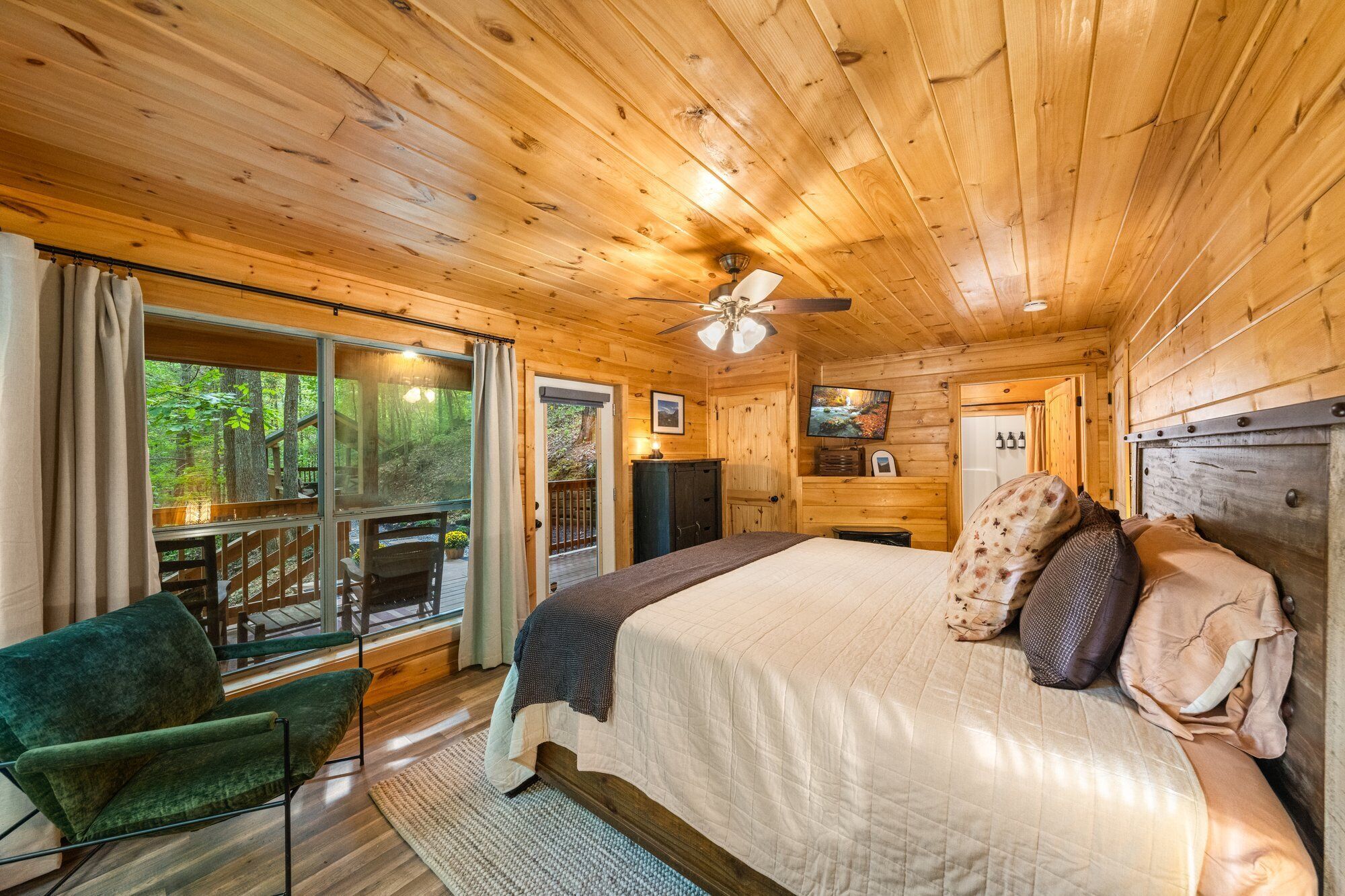 A wooden cabin bedroom with a bed, a chair, a TV, and a ceiling fan.