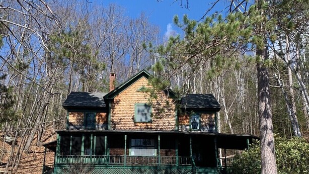 A two-story log cabin with a green porch and a chimney, surrounded by trees. - White Mountain Cottage, Birchcliff (Shelburne)