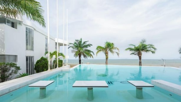 Ein moderner Poolbereich mit freiem Blick auf den Ozean, umgeben von Palmen und einem weißen Gebäude.