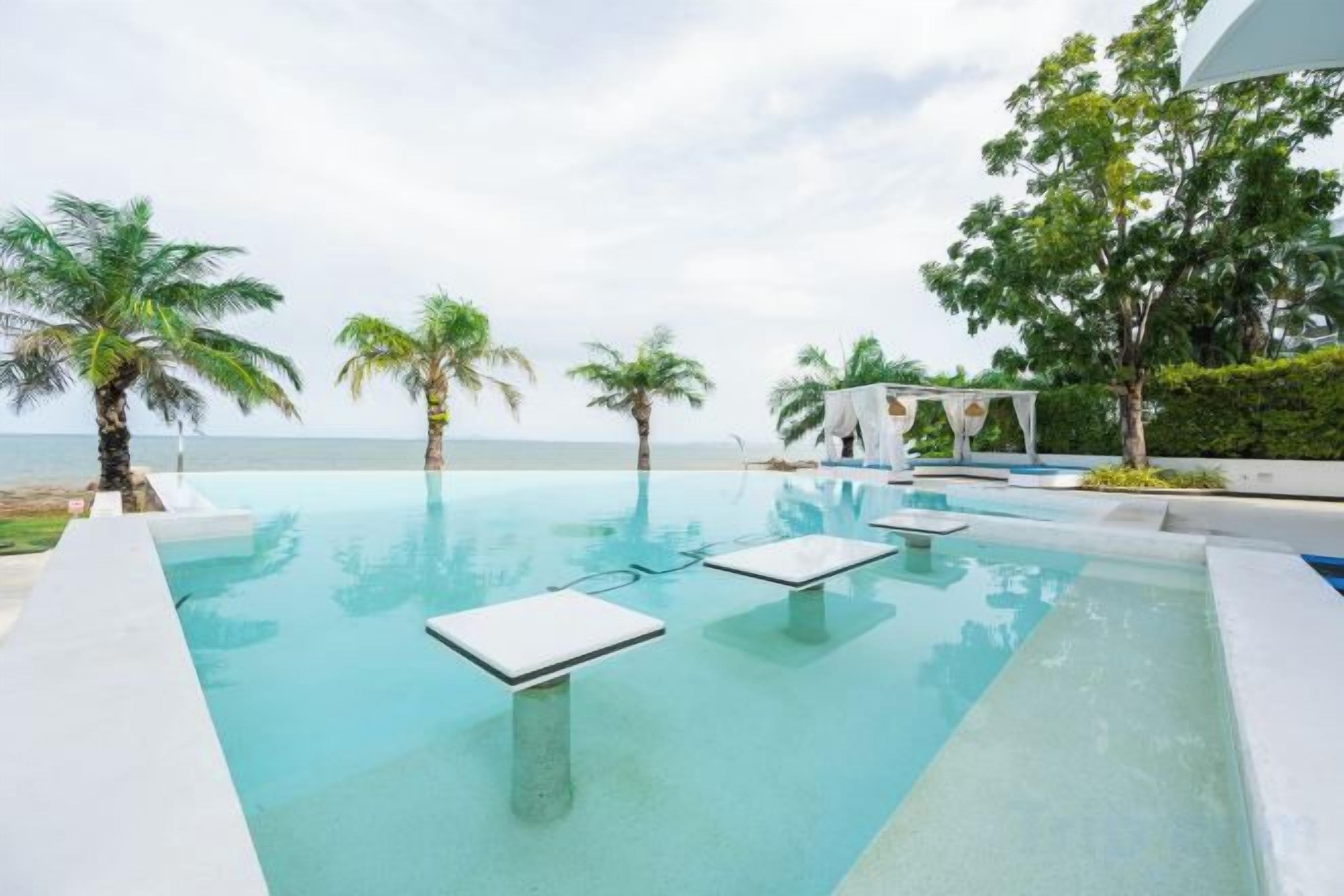 An infinity pool with a view of the sea, surrounded by palm trees and a white structure.