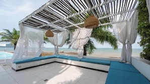 Eine Strandlounge mit weißem Baldachin, blauen Kissen und Blick auf das Meer.