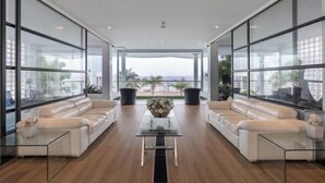 Ein großzügiger Wohnbereich im modernen Design mit einem Glastisch, zwei Sofas und großen Fenstern mit Blick ins Freie.