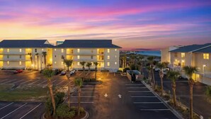 A hotel with a parking lot, multiple buildings, and palm trees. - Seaside Escape | Pool • Ocean Views • Family Ready (Navarre)