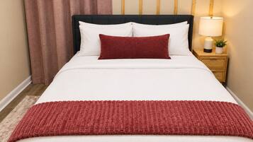 A bed with white bedding and a red throw blanket, a wooden nightstand with a lamp, and a wooden headboard.