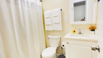 Un baño con inodoro, lavabo, espejo, cortina de ducha y un cubo de basura.