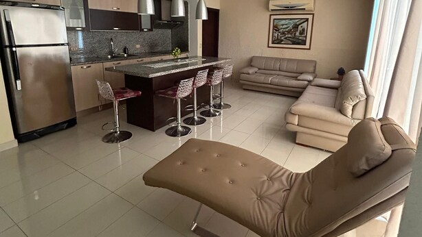 Um espaço moderno para viver, com cozinha, sala de jantar e área de estar com sofá e apoio para os pés.