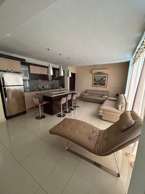 A modern living space with a kitchen, dining area, and a lounge area with a sofa and ottoman.