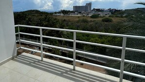 Varanda com guarda-corpo de metal com vista para uma paisagem montanhosa e edifícios ao longe.