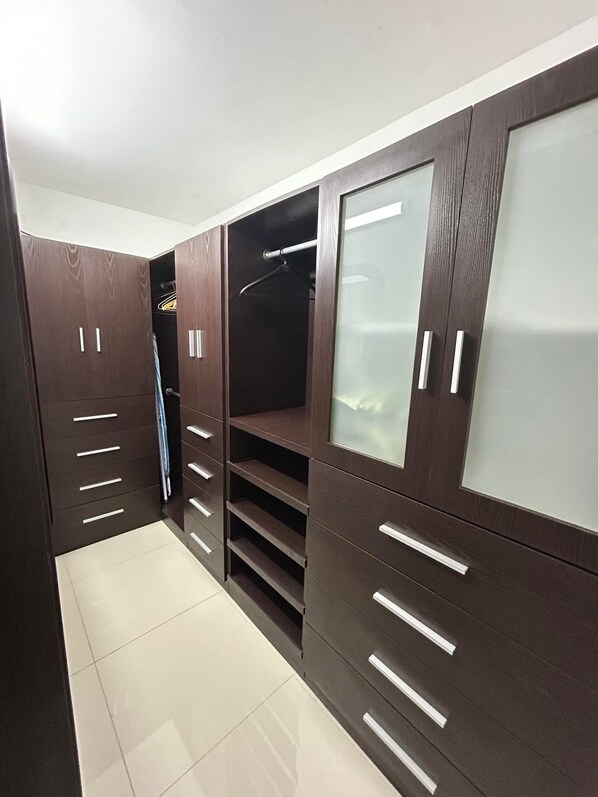 A walk-in closet with dark wood cabinets, multiple shelves, and a mirrored closet door.