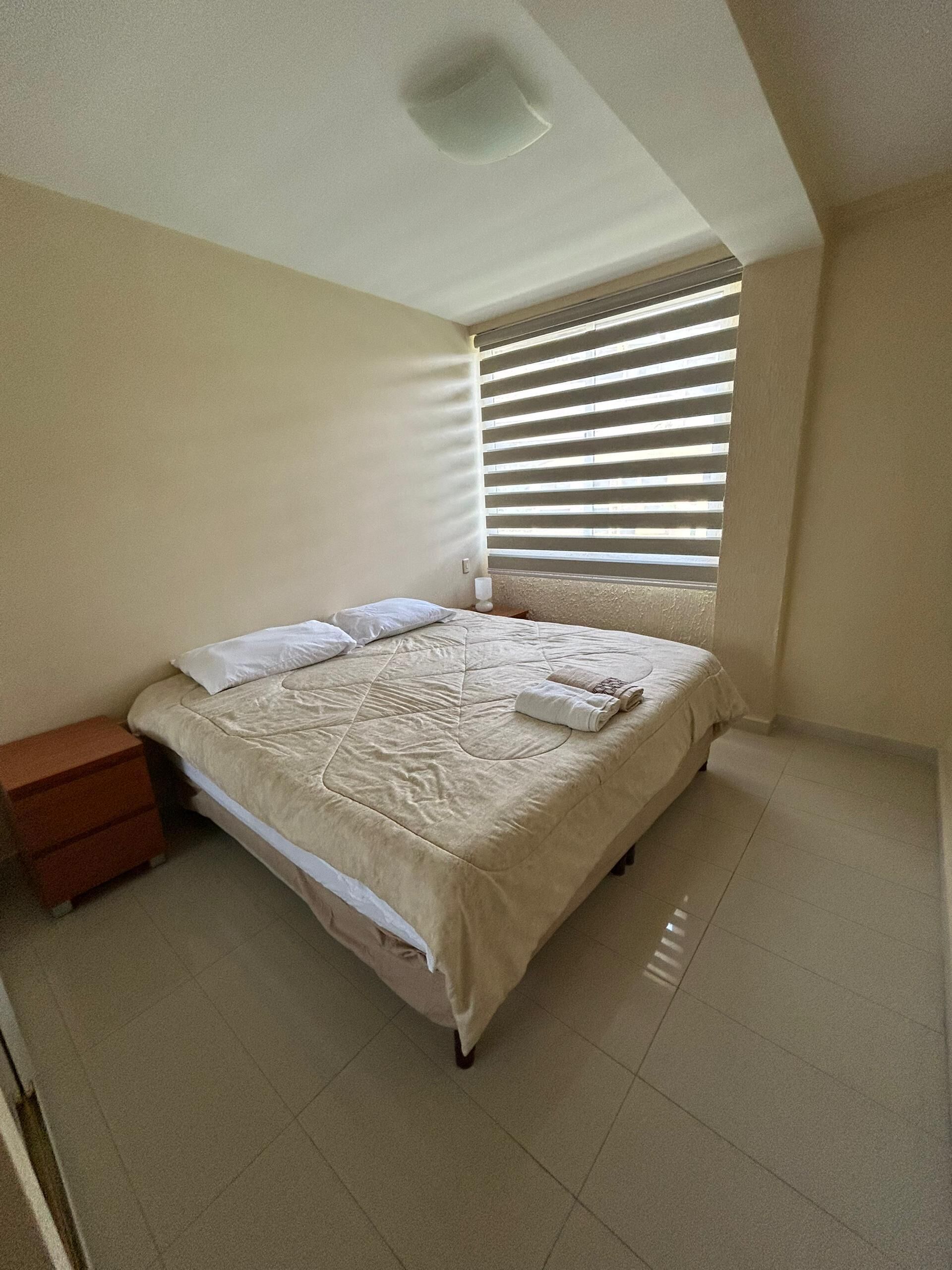 A bedroom with a bed, a nightstand, and a window with blinds.