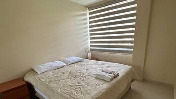 A bedroom with a bed, a nightstand, and a window with blinds.
