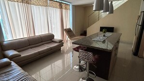 Uma sala de estar moderna com um sofá, uma área de jantar com um banquinho de bar e uma cozinha com geladeira.