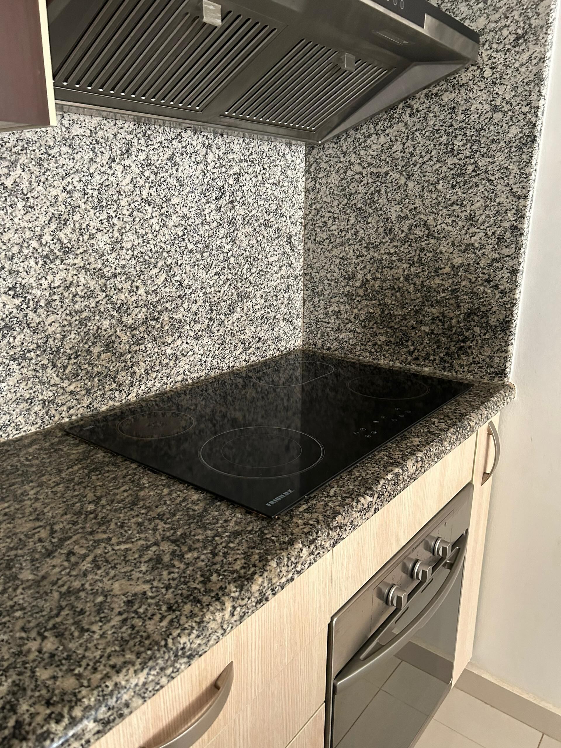 Una cocina con encimera de granito, placa de inducción negra y horno de acero inoxidable.