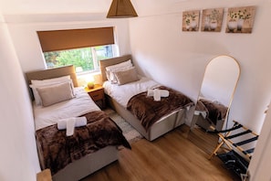 A compact room with two beds, a small table, and a window with a view of greenery. - 3Bedroom-Sleeps5-WiFi-SingleCarParking (Manchester)