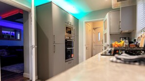 A modern kitchen with grey cabinets, a built-in oven, and a countertop with a coffee maker and fruit basket. - 3Bedroom-Sleeps5-WiFi-SingleCarParking (Manchester)