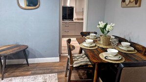 A dining area with a wooden table set for four, a mirror, and a kitchen in the background. - 3Bedroom-Sleeps5-WiFi-SingleCarParking (Manchester)