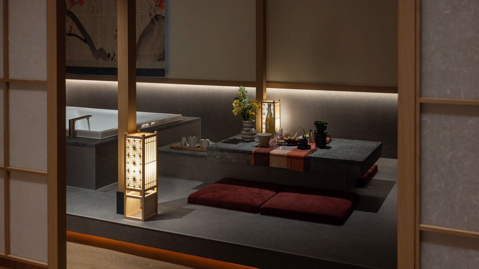A traditional Japanese-style room with tatami flooring, a low table with a vase of flowers, a tea set, and a lantern.