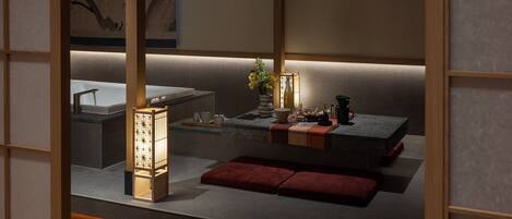 A traditional Japanese-style room with tatami flooring, a low table with a vase of flowers, a tea set, and a lantern.